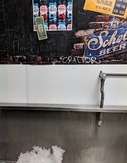 A wet dollar stuck to the wall above the trough