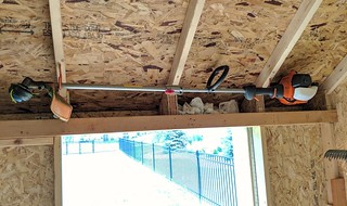 Snuck the weed eater in above the door with some old bike hooks