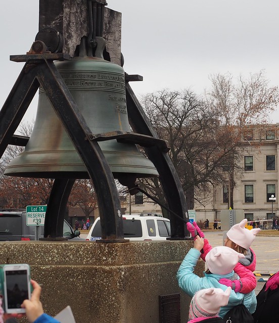 A little girl ringing the bell at the capitol with her mom